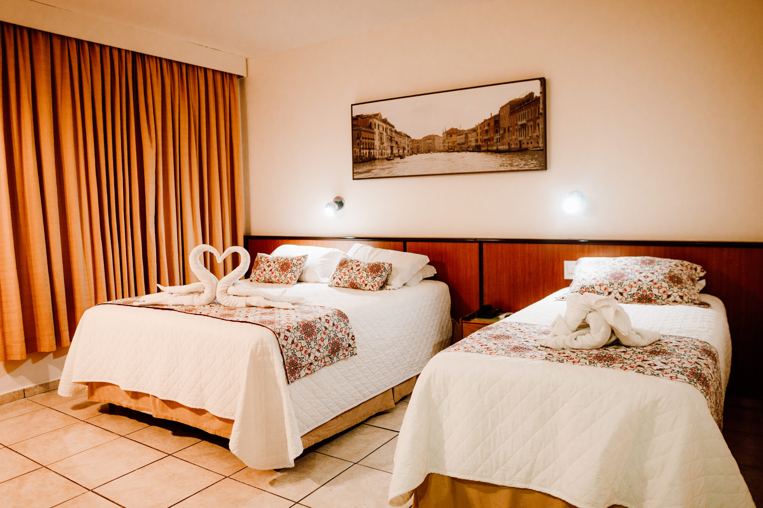 Quarto aconchegante com duas camas decoradas, cortinas fechadas e iluminação suave, ideal para hospedagem confortável.